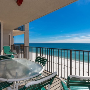 Relax at the round table with green chairs, enjoying views of the calm water and beach from your spacious balcony
