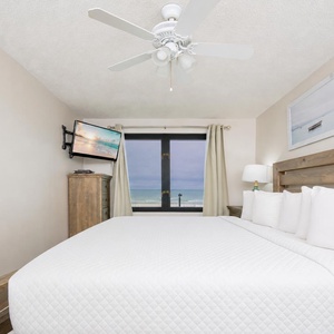 This bedroom features a cozy bed, a mounted TV, and a stunning beachfront view from the large window