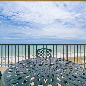 Balcony features a round wooden table and chairs, offering a serene view of the beach and gentle waves beyond