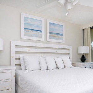 This bedroom features a plush white bed, coastal artwork, and a stunning beachfront view from the large glass doors