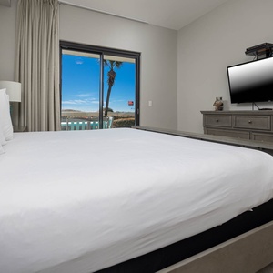Inviting master bedroom features a plush king bed, a mounted TV, and a sliding patio door revealing a lovely view