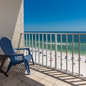 Enjoy a relaxing view from the balcony with blue chairs overlooking the sandy beach and vibrant umbrellas