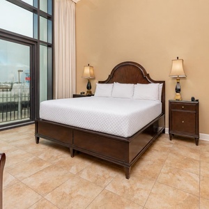 The master bedroom features a plush king bed, warm wood accents, and balcony access with beachfront views