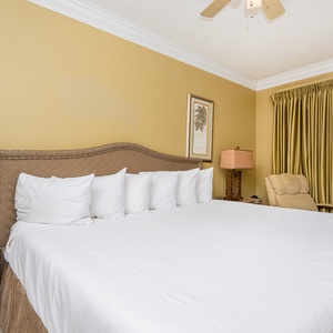 Spacious master bedroom features a king bed with white linens, a cozy armchair, and access to a balcony with gulf views