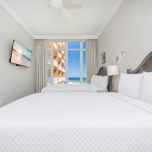 Relax with your favorite show and a stunning beach view from this guest bedroom with two queens