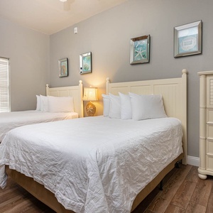 Bright guest bedroom featuring two queen beds, soft linens, and coastal decor, creating a relaxing atmosphere for vacationers