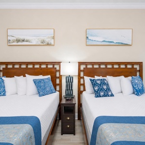 Guest suite with cozy queen beds invites restful sleep beneath coastal-inspired artwork and soft lamp glow