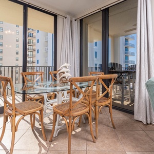 Bright dining area features a glass table surrounded by wooden chairs, with views of the balcony and the beach beyond
