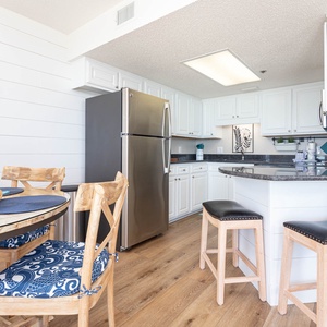 Bright and airy kitchen area featuring a breakfast bar with two stools, modern cabinetry, and a stylish dining table