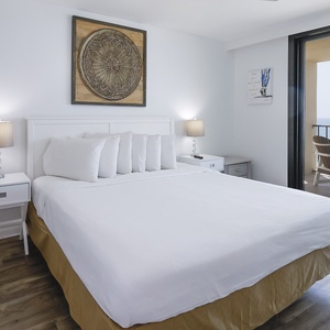 Master bedroom featuring a king bed with multiple pillows, a stylish lamp, and a sliding door leading to the balcony