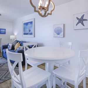 A cozy living area features a blue sofa with queen sleeper, a round white dining table, and nautical-themed artwork