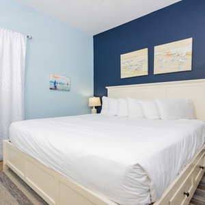 Serene guest bedroom features a plush king bed, soft blue walls, and nautical-themed artwork, creating a calming retreat