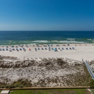 A vibrant beach scene features colorful umbrellas and sunbathers on white sand, framed by gentle waves and a clear blue sky
