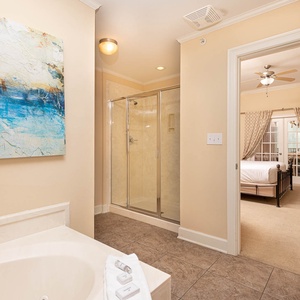 The master bath features a relaxing soaking tub, a glass walk-in shower, and a view into a cozy bedroom with soft beige tones