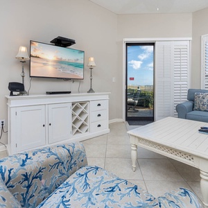 Cozy living area features a light blue sofa, patterned armchair, and a TV, with a view of the outdoor seating area