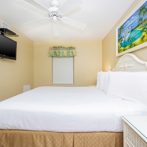 Brightly decorated guest bedroom features a queen bed, wall TV, and a window with colorful valance, creating a cheerful vibe