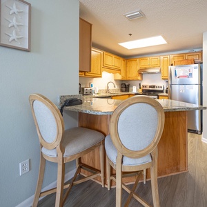 Breakfast bar with two stools complements the warm wood cabinetry and granite countertops in this inviting kitchen area