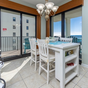 Bright dining area features a white table with seating, accented by coastal decor and a view of the gulf from the balcony
