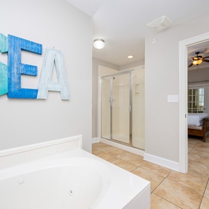 The master bath features a jetted tub, a glass walk-in shower, and charming decor, enhancing your coastal retreat experience