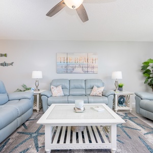 The living area features light blue leather sofas, a decorative rug, and beach-themed artwork, inviting relaxation