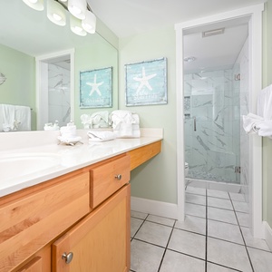Bright master bathroom featuring a spacious vanity, decorative starfish art, and a walk-in shower with elegant marble accents
