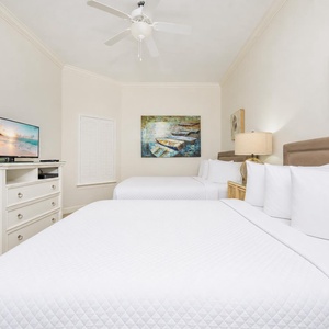 Inviting guest bedroom with two comfy queen beds, a TV, and beach-themed artwork for a relaxing getaway