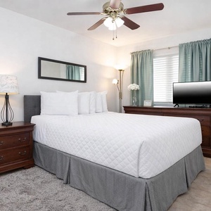 This cozy bedroom features a plush bed, a TV for entertainment, and soft, natural light from the window