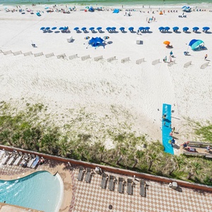 Relax by the gradual entry pool with a waterslide, enjoying the vibrant beach scene with colorful umbrellas
