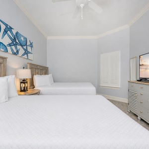 Bright and airy guest bedroom featuring two cozy queen beds, a large TV, and beach-themed decor for a relaxing getaway