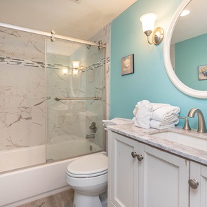 This bathroom features a stylish marble shower, a spacious vanity with elegant fixtures, and a calming turquoise accent wall