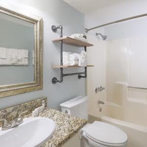 This bathroom features elegant granite countertops, stylish shelving, and a relaxing tub for a refreshing getaway experience
