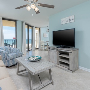 Bright living area featuring a cozy sofa, patterned armchair, and a TV, with expansive views of the beachfront