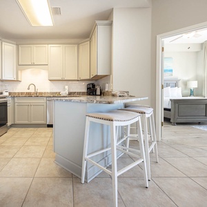 Modern kitchen features light cabinetry, a breakfast bar with seating, and a view into the inviting master bedroom beyond