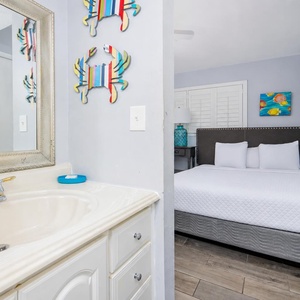 This bathroom features a stylish sink area with a large mirror, leading to a cozy bedroom adorned with colorful decor