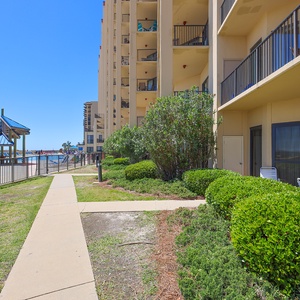 The outdoor area features well-maintained landscaping, a pathway leading to the pool area, and a view of the beach