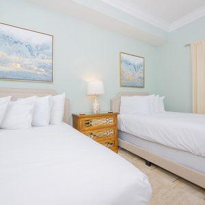 Two neatly made double beds with white linens, decorative artwork, and a wooden nightstand create a serene guest room vibe