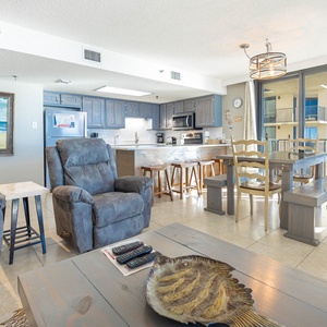 Living area features two recliners, a dining table, and a well-equipped kitchen with blue cabinetry and a breakfast bar