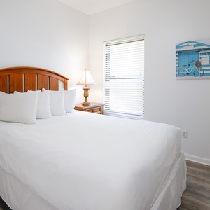 Bright and inviting guest bedroom featuring a cozy wooden queen bed, soft white linens, and a charming beach-themed artwork
