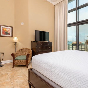 The master bedroom features a comfortable king bed, a TV for entertainment, and balcony access with beach views