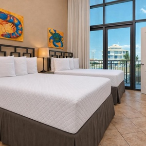 This bright guest bedroom features two full beds, vibrant coastal artwork, and large windows for a refreshing view