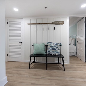 Welcoming entryway features a black bench with decorative pillows and a paddle on the wall, leading to a guest bedroom