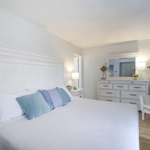 The bedroom features a serene atmosphere with soft blue accents, a cozy white bed, and stylish furnishings for a restful stay