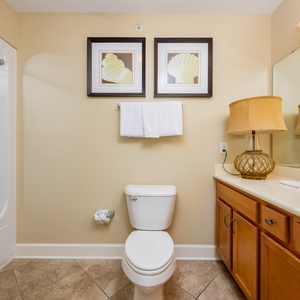 This bathroom features a stylish design with a tub shower combo, elegant shell artwork, and warm wood cabinetry