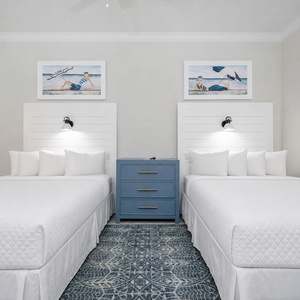 Inviting guest room featuring two comfortable queen beds adorned with coastal art and stylish reading lights