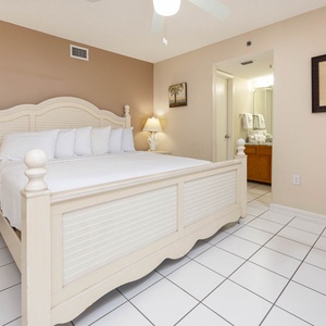 The master bedroom features a king bed with plush pillows, a bedside lamp, and an adjoining bathroom area