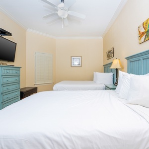 This cozy bedroom features two queen beds, a mounted TV, and charming aqua cabinetry, perfect for a relaxing stay