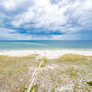 Expansive view of the beach with white sand, dotted with colorful umbrellas and loungers, leading to the tranquil gulf