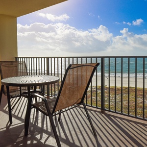 Balcony seating offers a relaxing spot to enjoy views of the beach and gentle waves under a bright, sunny sky