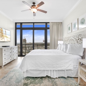 The master bedroom features a large window with a stunning view, king bed, a wall-mounted TV, and elegant white decor
