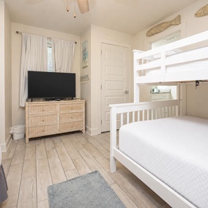 Bright guest room featuring a twin/double bunk bed, a double bed, TV, and light wood flooring, creating a welcoming vibe